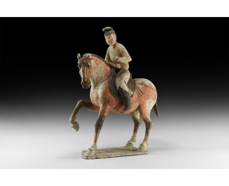 Tang Dynasty, 618-906 AD. A ceramic horse and rider figure on an irregular base, the horse advancing with one foreleg raised,