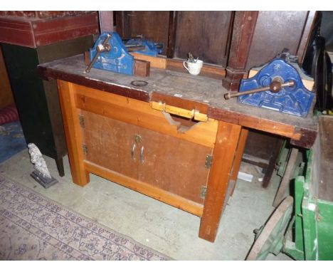 A traditional work bench with hardwood top and enclosed base together with two record vices