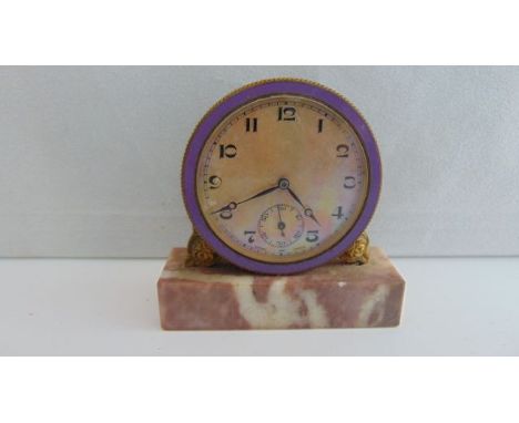A small vintage travel clock set on a polished marble base, lilac enamel bezel and opalescent dial , set within a simulated c