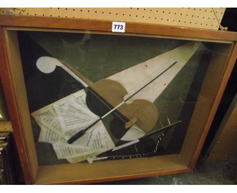 A glazed wooden display case containing a montage of sheets of music and a violin bow displayed against a collage background 