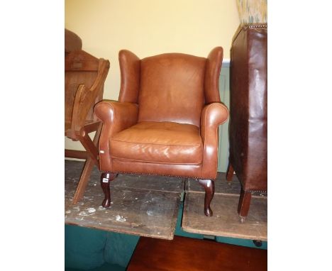 A Georgian style wing chair upholstered in a light tan leather upholstery, raised on short cabriole supports (Laura Ashley, D