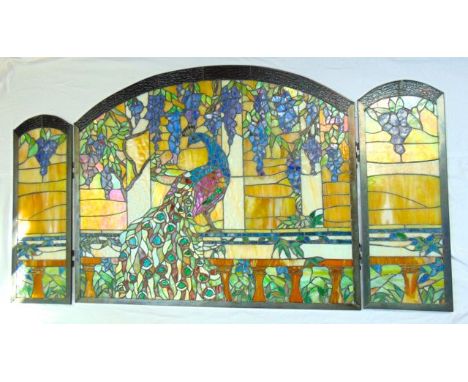 A contemporary leaded light three fold fire screen composed from segments of stained glass depicting a standing peacock set b