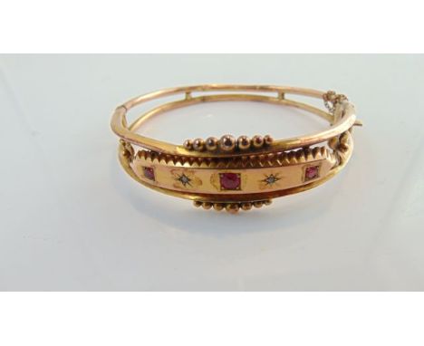 An Edwardian bangle, set with three graduated pink stones, possibly ruby, interspersed with two diamond chips, in 9ct gold, w
