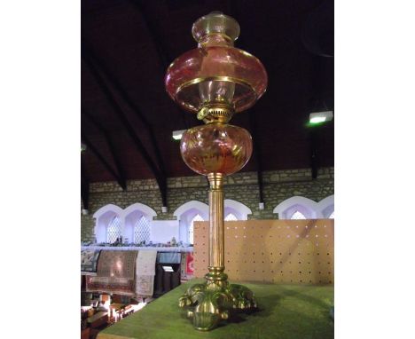 An oil burning lamp raised on a brass base with fluted column and cranberry tinted glass fount and further cranberry tinted s