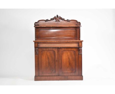 A late Victorian mahogany chiffonier, the shaped back carved with foliate scroll cresting over a narrow serpentine shelf rais