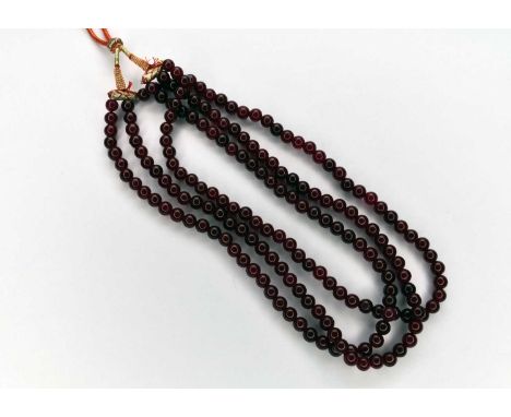 A three strand polished bead treated ruby necklace, with adjustable toggle cord fastening