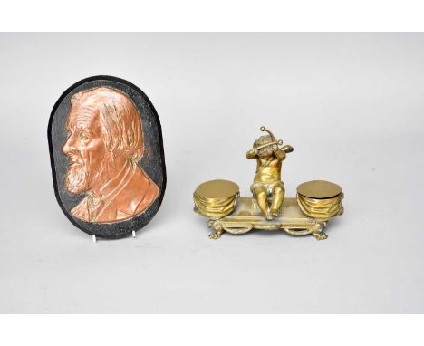 A cast brass figural desk standish, modelled as a putti flanked by two inkwells formed as drums, his arms raised with drumsti