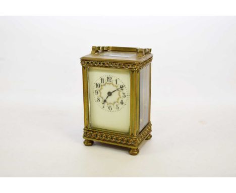 A French brass cased carriage clock, the case with chain-link decoration and raised on cushion feet, the off-white enamelled 