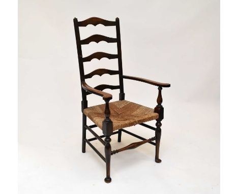 An oak ladder back rush seated open armchair, with shaped splats between turned rails, scroll arms on baluster supports over 