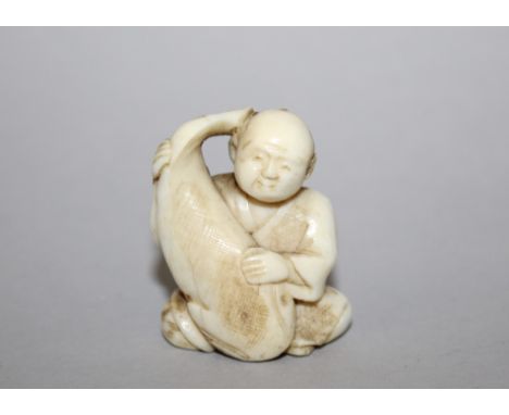 AN EARLY 20TH CENTURY SIGNED JAPANESE IVORY NETSUKE, carved in the form of a seated man holding a giant carp, the underside w