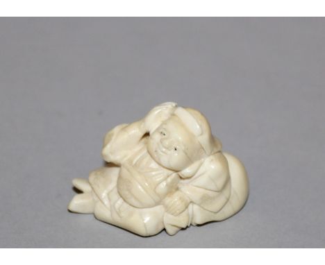 AN EARLY 20TH CENTURY JAPANESE CARVED IVORY NETSUKE OF DAIKOKU, unsigned, the deity reclining on his bag, 1.7in long & 1.1in 