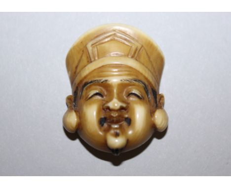 A JAPANESE MEIJI PERIOD STAINED IVORY MASK NETSUKE OF DAIKOKU BY IKKO, some of the details engraved and stained black, the un