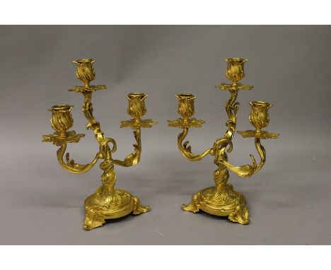 A GOOD PAIR OF LOUIS XVI ORMOLU THREE LIGHT CANDLESTICKS with acanthus decoration and circular bases 12ins high.