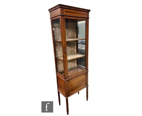 An Edwardian inlaid mahogany display cabinet of narrow proportions, the fitted shelf interior enclosed by a glazed door on tu