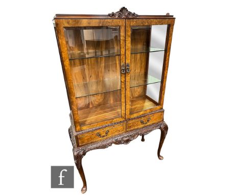 A Queen Anne style carved figured walnut two door display cabinet, the glass shelf interior enclosed by a pair of glazed door