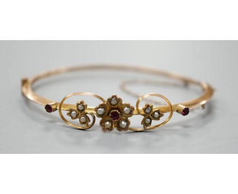 An Edwardian 9ct, red stone and seed pearl set hinged bangle, interior diameter 55mm, gross weight 4.4 grams.