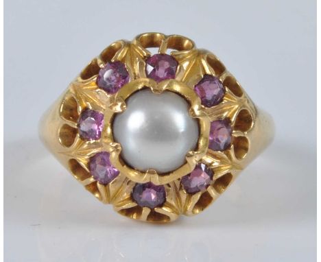 A yellow metal, pearl and ruby heavy circular cluster ring, featuring a centre 7.3mm cultured pearl within a border of eight 