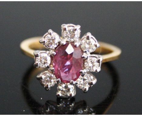 An 18ct yellow and white gold, ruby and diamond oval cluster ring, featuring a centre oval faceted ruby within a border of 8 