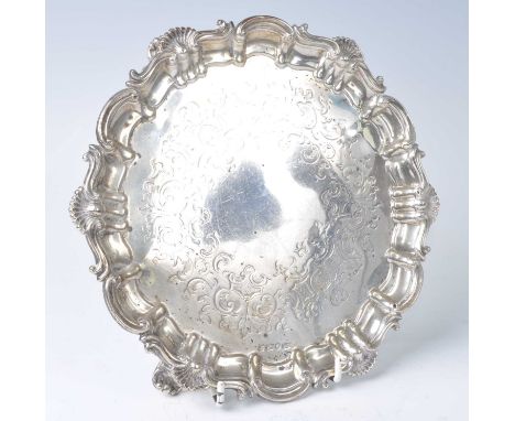 A mid-Victorian silver salver, of shaped circular form with shell and scrolling rim and engraved centre, standing on three sc