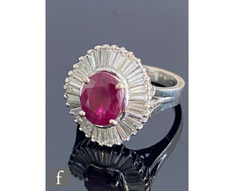 An 18ct white gold ruby and diamond cluster ring, central oval claw set ruby, length 9mm, within a waved border of thirty two