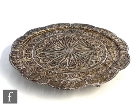 A Middle Eastern low grade filigree silver circular salver decorated with foliate scrolls and raised on three fan style feet,