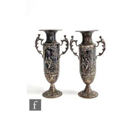 A pair of hallmarked silver twin handled bud vases each with embossed figures in a landscape setting below flaring borders, h