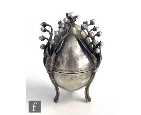 A Russian silver modelled of an egg, raised on three strut legs and detailed with faux pearls, opening to reveal a figure of 