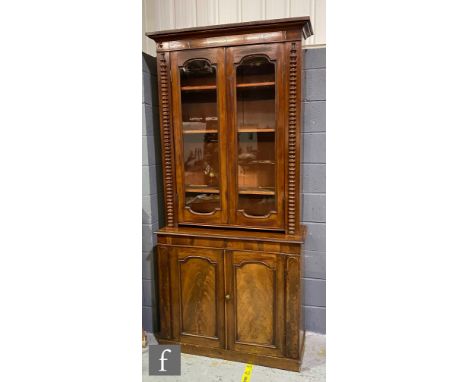A Victorian mahogany floorstanding bookcase enclosed by a pair of glazed doors flanked by bobbin pilasters over a cupboard pl