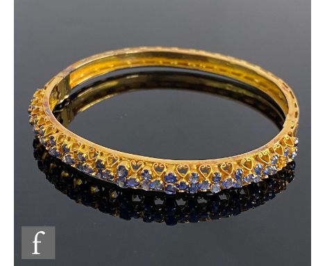 An 18ct hinged bangle detailed with claw set sapphires to scroll setting with foliate engraved decoration to back section, to