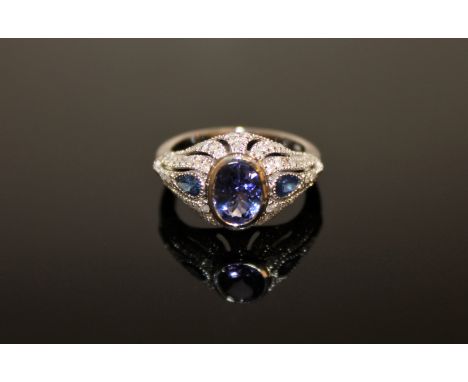 A 14ct white gold tanzanite, sapphire and diamond Art Deco style ring, the oval-cut tanzanite weighing 1.10 carat, between tw