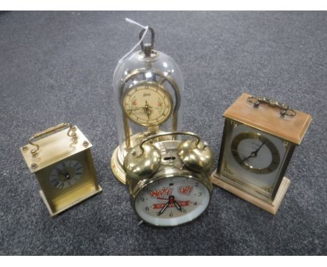A Schatz anniversary clock under shade together with two mantel clocks and an alarm clock