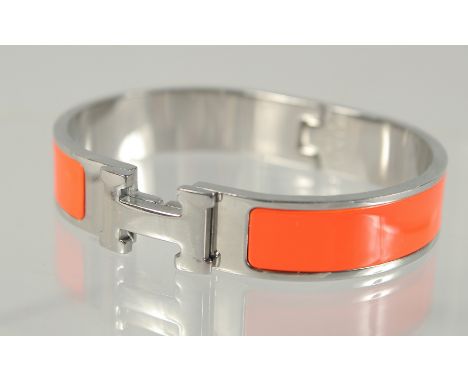 A HERMES ORANGE AND CHROME BANGLE.