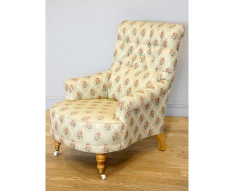 A Victorian style upholstered armchair, with button back and scroll arms, the front legs raised on porcelain casters, 75 x 85