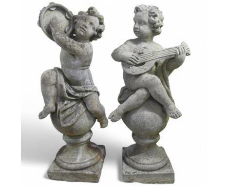 A pair of weathered concrete garden statues in the form of Putti sat on spherical acorn finials playing musical instruments. 