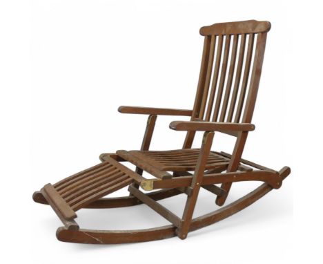 A weathered teak rocking steamer chair with folding footrest and adjustable back cushion.