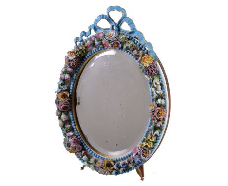 An English porcelain flower encrusted oval looking glass frame with wood easel stand, surmounted with a blue ribbon bow, late