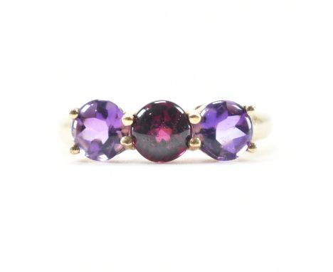 A hallmarked 9ct yellow gold, amethyst &amp; garnet three stone ring. The ring having a central magenta garnet cabochon flank