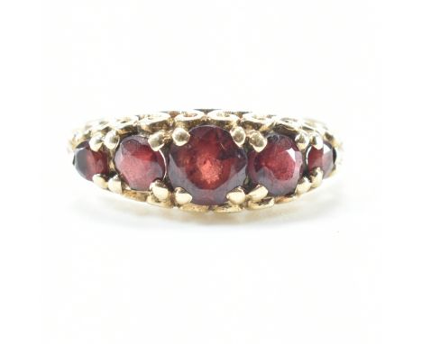 A 9ct gold and garnet five stone ring. The ring set with five graduating round cut garnets to pierced and scrolled gallery. H