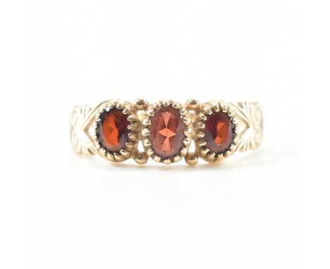 A hallmarked 9ct yellow gold &amp; garnet three stone ring. The ring having three graduated oval cut garnets to split scrolli