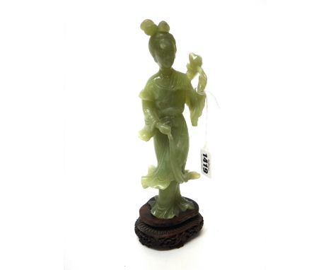 A Chinese celadon jade figure of a woman, late 19th/20th century, standing in long robes holding a lotus flower in one hand, 