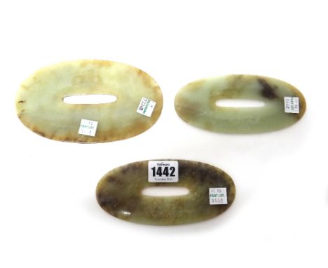 Three Chinese green and brown jade graduated oval pierced discs, each carved with a mask, 14cm. to 17cm. wide.