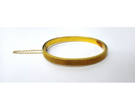 A gold oval hinged bangle, the back and the front with cross hatched decoration, on a snap clasp, fitted with a safety chain,