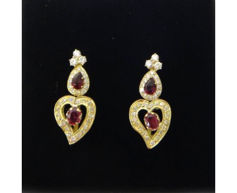 A pair of gold, ruby and diamond pendant earrings, each drop mounted with an oval cut ruby to the centre, within a heart shap