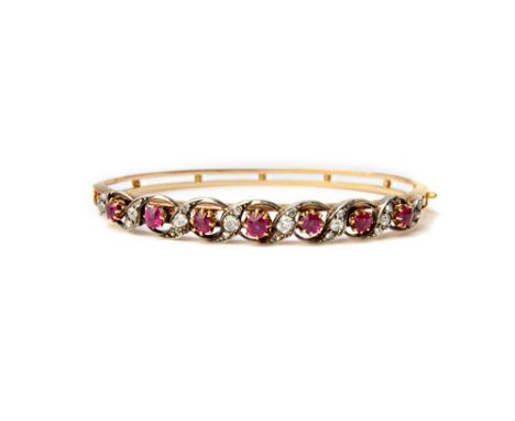 A gold and silver set, ruby and diamond set oval hinged bangle, the front pierced in a scrolling design, mounted with a row o