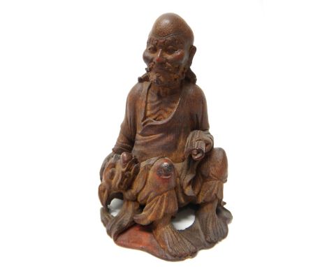 A Chinese bamboo figure of a luohan, carved seated holding a scroll in his left hand, a Buddhist lion at his side, 19cm. high