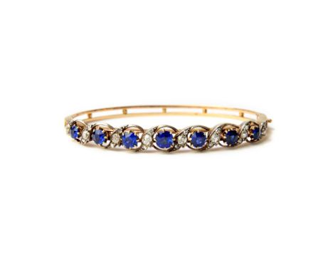 A gold and silver set, sapphire and diamond set oval hinged bangle, the front pierced in a scrolling design, mounted with a r