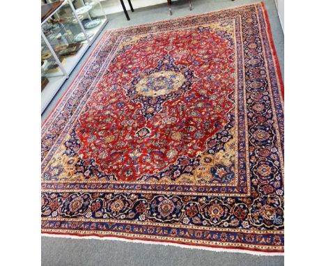 An Isfahan carpet, the brick red main field with symmetrical floral sprays around camel and dark blue stepped lobed medallion