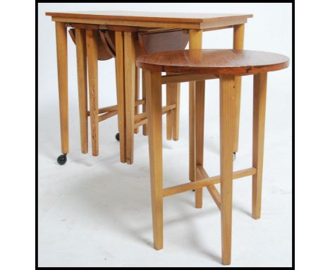 A vintage mid 20th century teak side - nest of tables with a trio of slide out metamorphic round teak occasional tables raise