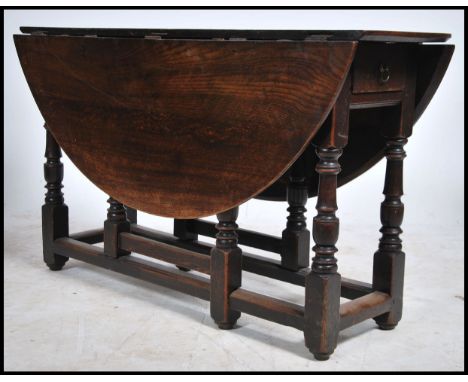 An 18th century country oak drop leaf / gate leg dining table being raised on turned legs with pad feet having half moon drop