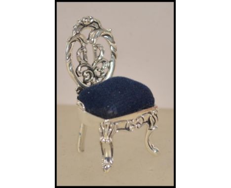 A silver pin cushion in the form of a Thomas Chippendale chair having blue baize cushion to the seat. Weight 8.8g. Measures 3